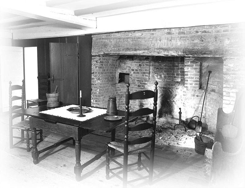 This interior photo of the oldest house in Nantucket shows a table with straight-back chairs drawn close to the massive fireplace.
